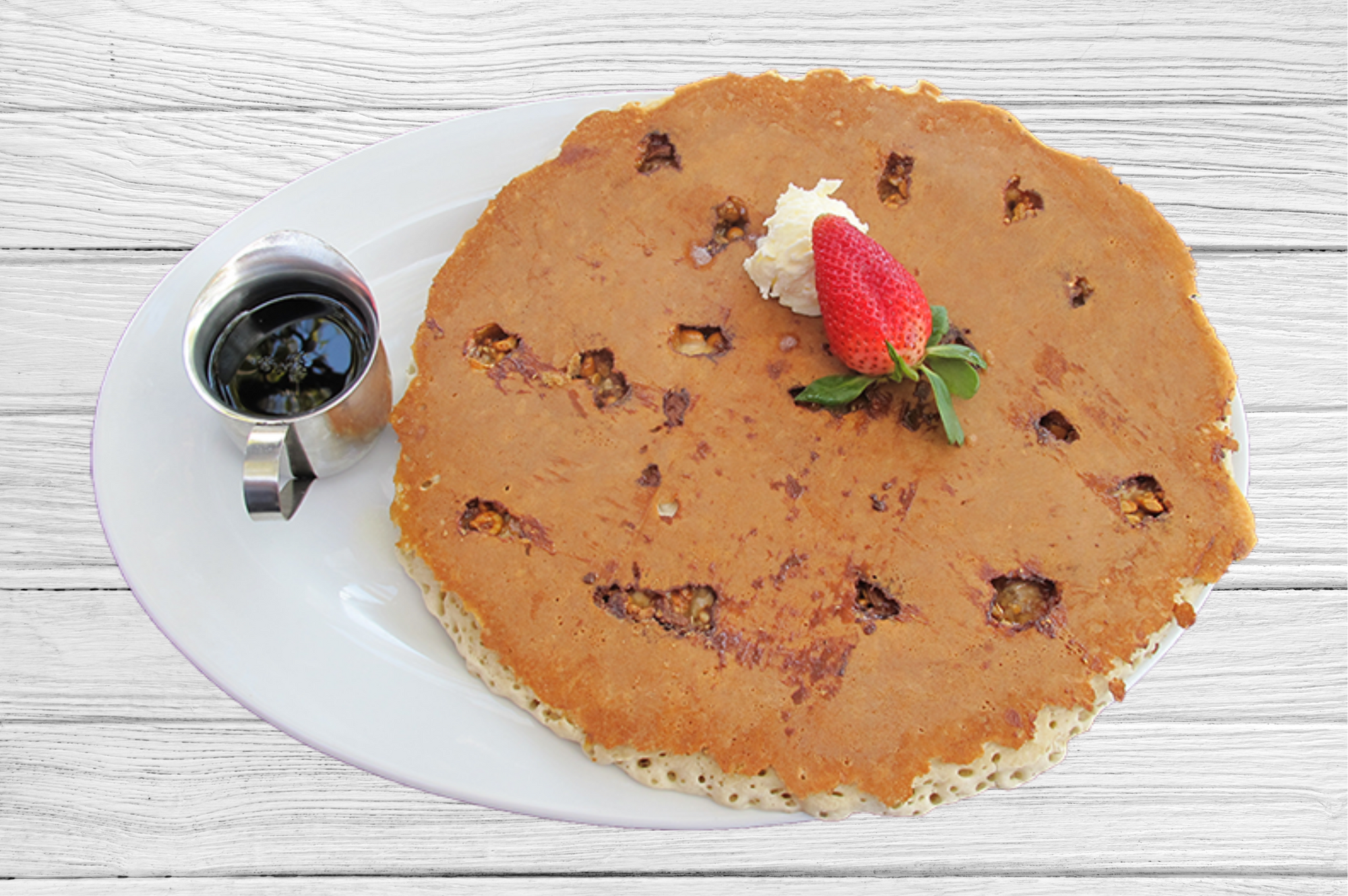 Big plates with a oversized pancake topped with whipped butter and strawberry, served with syrup on the side at Hash House A Go Go Mohegan Sun