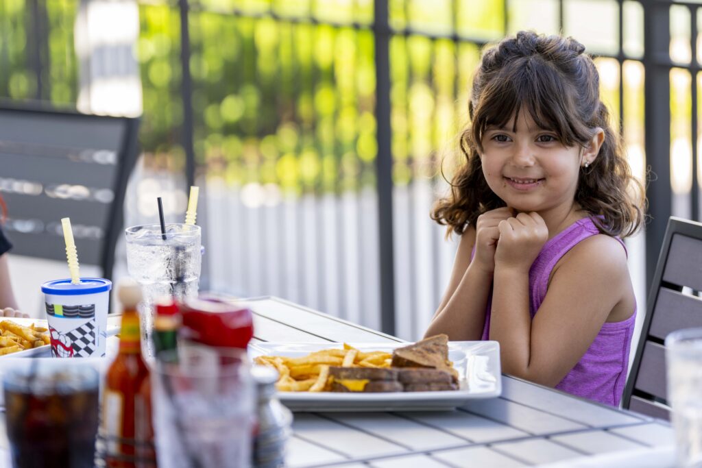 Smiling child enjoying a family meal with fries and a grilled cheese sandwich at Hash House A Go Go Mohegan.
