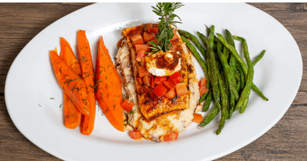 A healthy entrée from Hash House A Go Go Mohegan featuring grilled salmon over mashed potatoes, with steamed carrots and sautéed green beans.