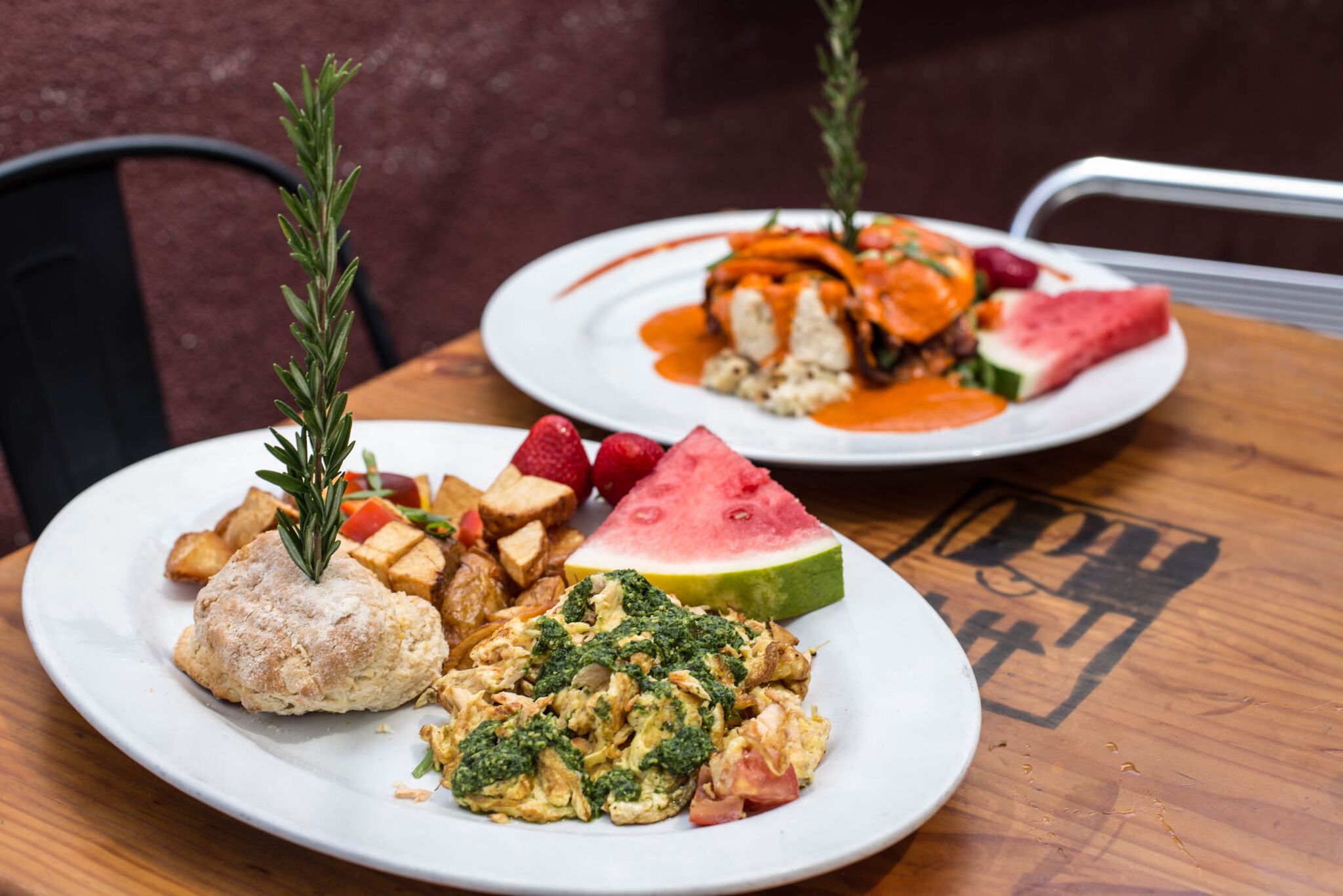 Two oversized brunch plates from Hash House A Go Go at Mohegan Sun featuring scrambled eggs, house biscuit, potatoes, fruit, and a stacked entrée with chipotle cream